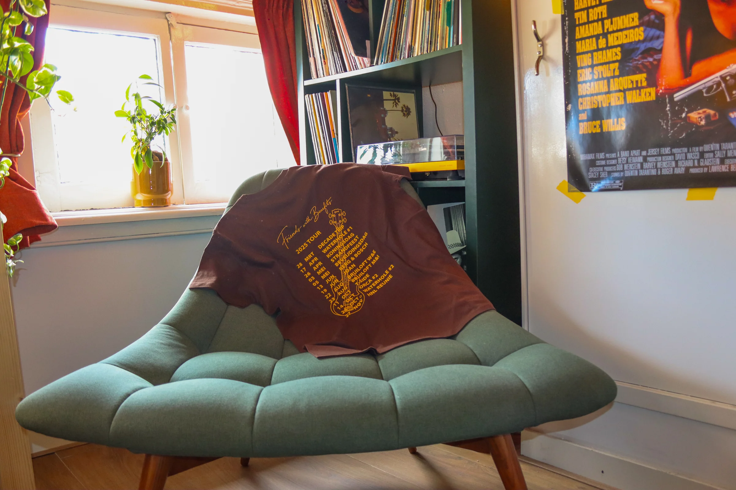 Ons bruine shirt met gele opdruk op een groene stoel, naast een kast vol platen